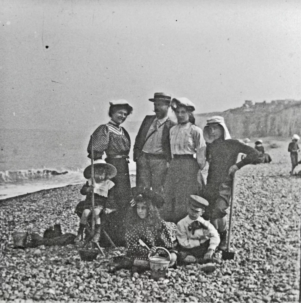 Deux femmes, un homme au canotier et quatre enfants avec seaux et pelles sur une plage de galets