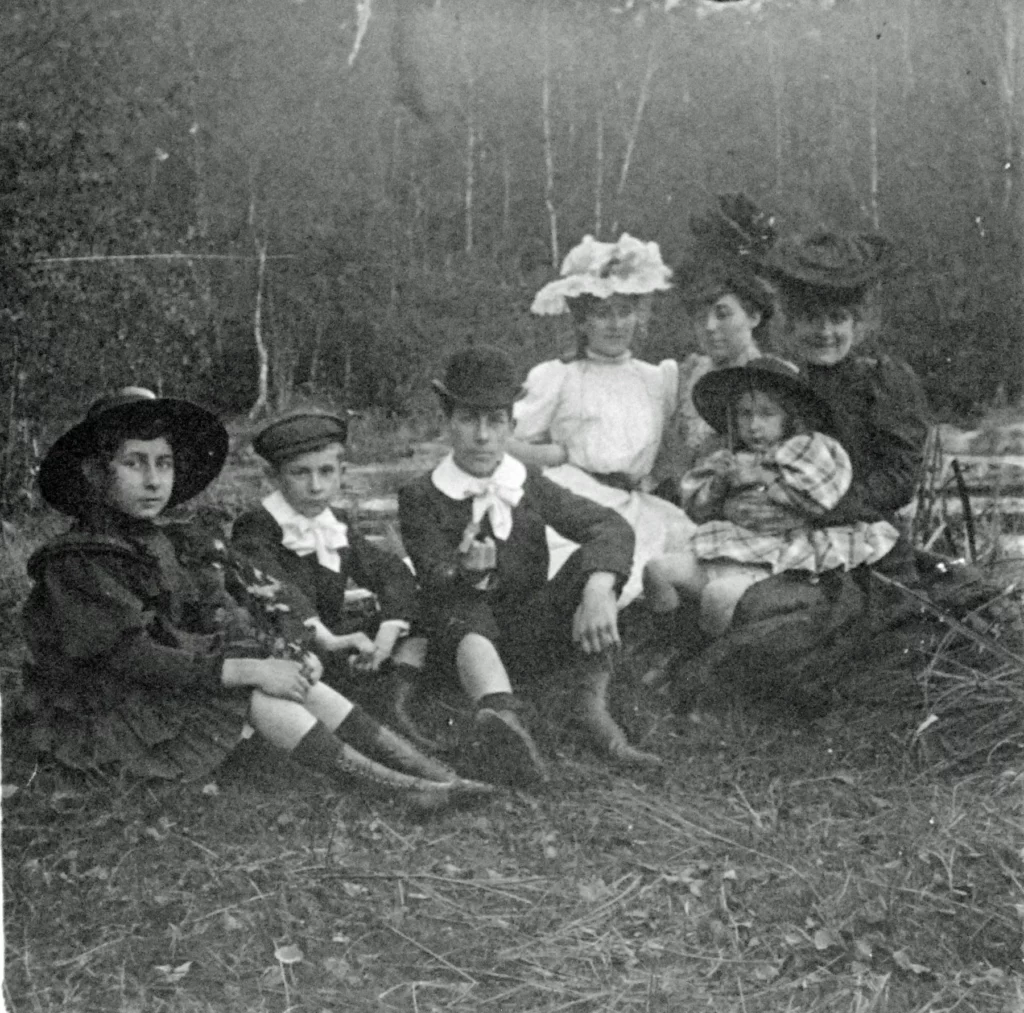Quatre enfants assis dans l'herbe, deux dames en chapeau et une fillette sur les genoux