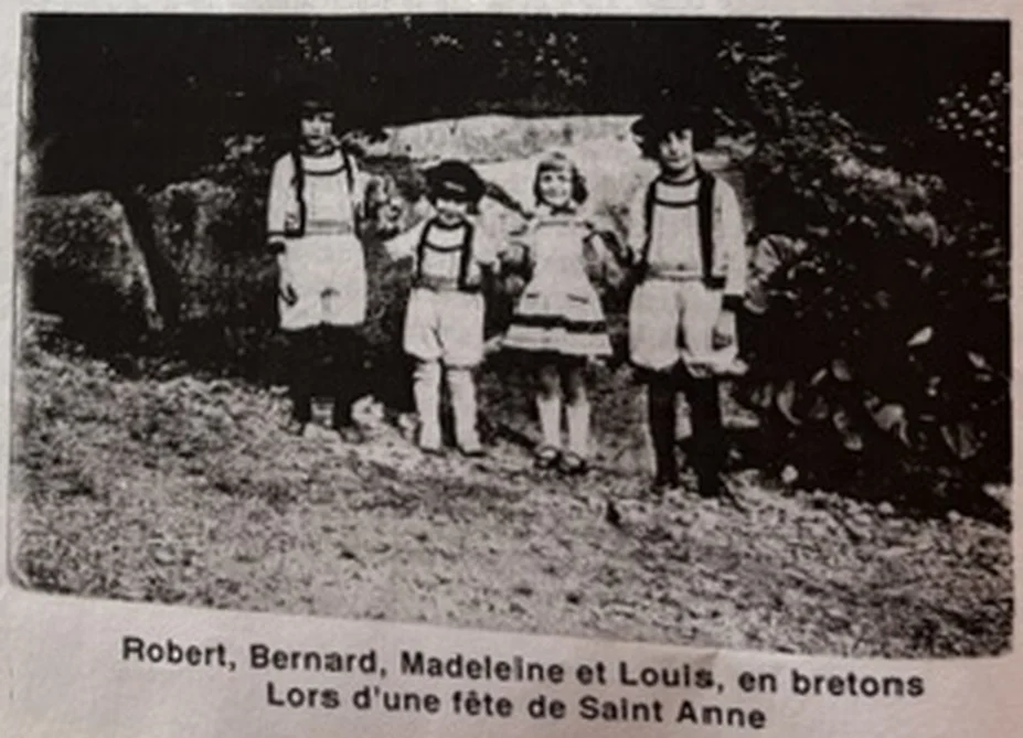 Quatre enfants en costume breton traditionnel devant un bosquet